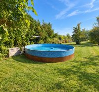 Outside in Martovce near a family house, a round pool on the lawn surrounded by greenery.