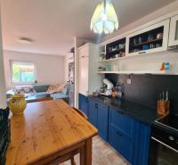 A kitchen in a family house with a wooden table, blue cabinets, and a sofa in the background.