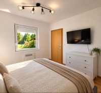 A bedroom in a family house with light furniture, a window, and a TV on the wall.