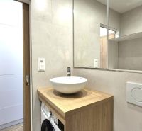 A bathroom in a studio apartment with a white sink, wooden decor, and storage baskets.