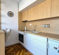 A kitchenette in a studio apartment with a wood-patterned floor and built-in appliances.