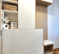 A studio apartment interior with wooden furniture, decorations, and a plant on a wooden-patterned floor.