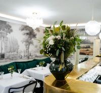 Interior of commercial spaces with a golden bar, floral decoration, and elegant tables.