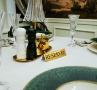 A reserved table with place settings in a business establishment, includes spice shakers and elegant glasses.