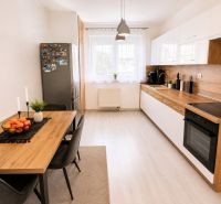 A kitchen in a 2-room apartment with a wooden decor floor, a dining table, and appliances.