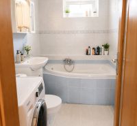 Bathroom in a 2-room apartment with a bathtub, washing machine, and light-colored tiles.
