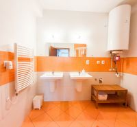 A bathroom in a 3-room apartment with orange tiles, two sinks, and a boiler.