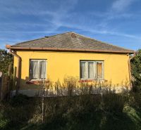 A yellow family house in Komárno with a fence and a garden under the blue sky.
