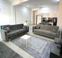 Living room with three gray sofas, a table, and a kitchen in a two-room apartment.