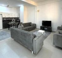 Modern living room in a two-room apartment with a large sofa and a kitchenette.