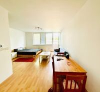 A one-room apartment with a wooden decor floor, with a bed and a work desk.