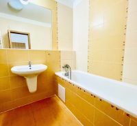 Bathroom in a studio apartment with a bathtub and a sink, light yellow tiles.