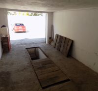 A garage with a service pit, an older concrete surface, and a parked car outside.