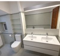 Bathroom in a family house with a double sink, toilet, and mirror.