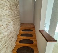 A narrow staircase with brown treads and a wall with a stone decor in a family house.