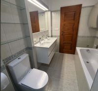 Bathroom with a bathtub and toilet in a family house, white tiles and wooden doors.