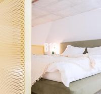 A bedroom in a two-room apartment with a bed and a yellow partition.