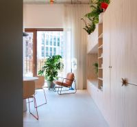 A bright interior of a 2-room apartment with plants, a comfortable armchair, and shelves.