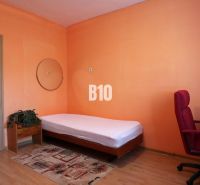 A room in a family house with a bed, a desk, and a wooden-decor floor.