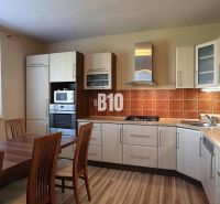 A kitchen with a corner unit, a wooden table, and a floor with a wooden decor.