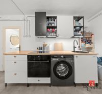 A kitchen in a 2-room apartment with a washing machine and a wooden decor countertop.