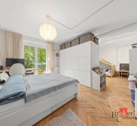 A bedroom in a two-room apartment with a wood-patterned floor, a large bed, and storage spaces.