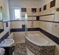 A bathroom in a family house with a bathtub, tiles, and a window; modest furnishings and a light fixture.