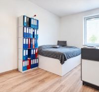 A bright room in a family house with a bed, a shelf for binders, and a floor with a wooden decor.