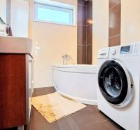 A bathroom in a family house with a bathtub, a washing machine, and dark tiles in a decorative design.