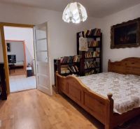 A bedroom in a family house with a wooden decor floor, a large bed, and a lamp.