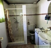Bathroom in a cottage with white tiles, a shower, and a sink with a mirror.