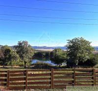 View of the lake from the garden in Krupina, surrounded by greenery and a wooden fence.