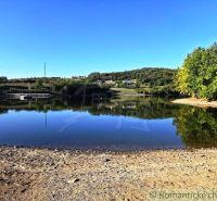 A peaceful body of water in the Gardens in Krupina surrounded by greenery and a blue sky.