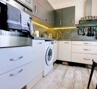 A kitchen with white and gray cabinets in a 2-room apartment, floor with wood decor.