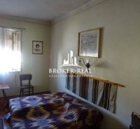 A room in a family house with a chair, a bed, and a wooden-patterned floor.