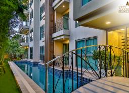 A swimming pool and the facade of a residential building in Pattaya surrounded by greenery.