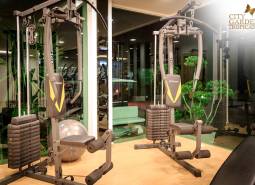 Fitness equipment in apartment construction, green elements, lighting, and mirrored walls.