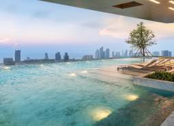 A pool with loungers and a view of the Pattaya city skyline from the apartment construction.