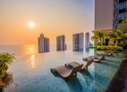 Pool, loungers, and the panorama of apartment construction in Pattaya at sunset.