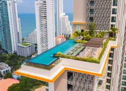 Apartment construction in Pattaya with a rooftop pool, with the sea and high-rise buildings in the background.