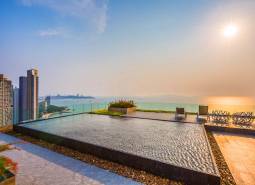 Apartment construction in Pattaya with a rooftop pool and sea view at sunset.