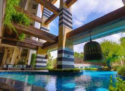 A luxurious pool with wooden beams, surrounded by greenery, falls under the construction of apartments.