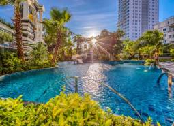 Apartment construction in Pattaya with a pool surrounded by greenery and palm trees in a sunny environment.