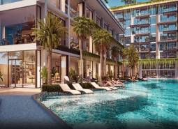 Apartment construction in Pattaya with a pool and loungers surrounded by palm trees and plants.