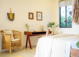A bright bedroom in a family house with a rattan chair and a wooden table.