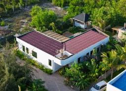 Construction of houses in Paje, Unguja South Region, with red roofs surrounded by greenery.