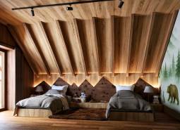 Attic bedroom with two beds, wooden decor, and a forest motif on the wall.