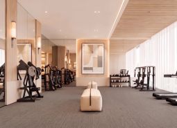 Fitness space with wood-patterned flooring, mirrors, and exercise equipment in an apartment development.