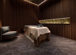 A room with a massage table, a wooden decor floor, and a comfortable armchair. Apartment construction.