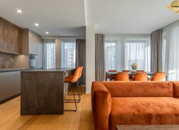 Interior with wood-patterned flooring, orange sofa, and dining table. Apartment construction.